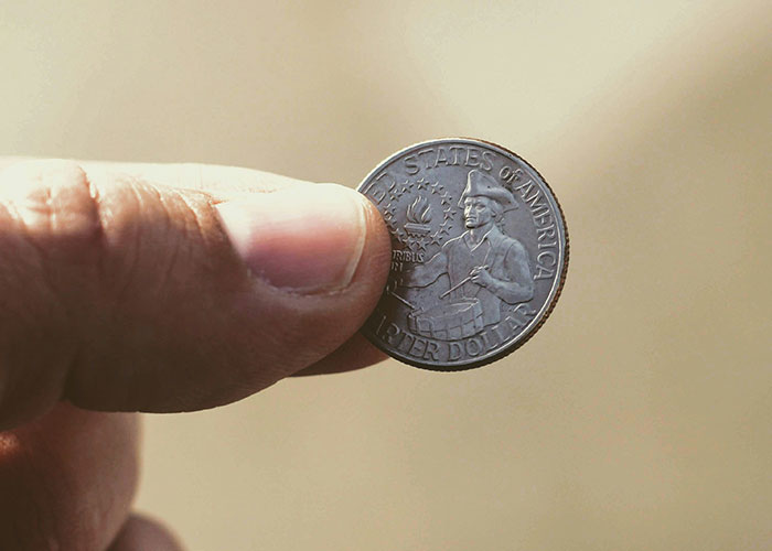 Close-up of a hand holding a U.S. quarter dollar coin, possibly highlighting strange human behavior.