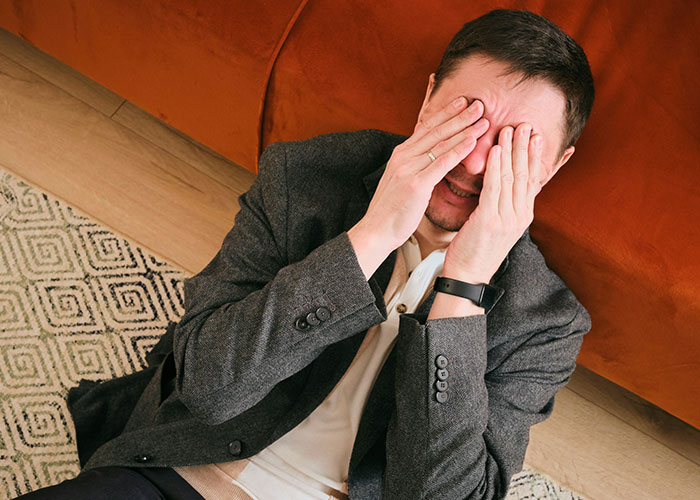 Man in a suit sitting on the floor, covering face, illustrating strange human behavior in a courtroom setting.