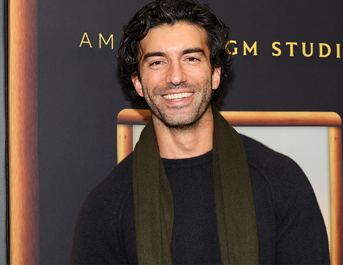 A person smiling at an event, wearing a dark shirt and green scarf, related to Intimacy Coordinator opinion.