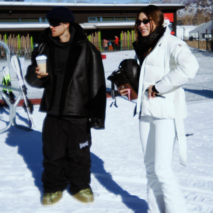 Snowy scene with Hailey Bieber in white outfit and Justin holding a coffee cup, both enjoying winter activities.