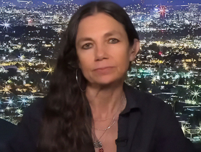 Woman speaking against a city skyline at night, discussing Prince Harry and Meghan Markle after LA fire victims visit.