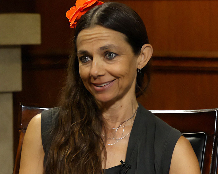 Woman with long hair and a red flower smiling at an interview, related to opinion on Prince Harry and Meghan Markle.