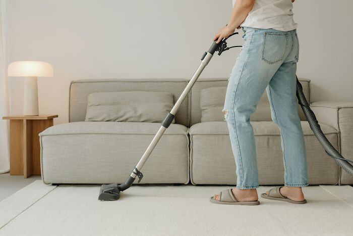 Person vacuuming a carpet in a living room, using an expensive item worth spending money on.