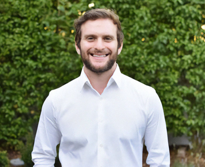 Man in a white shirt smiling outdoors, representing private firefighter services for wildfire protection.