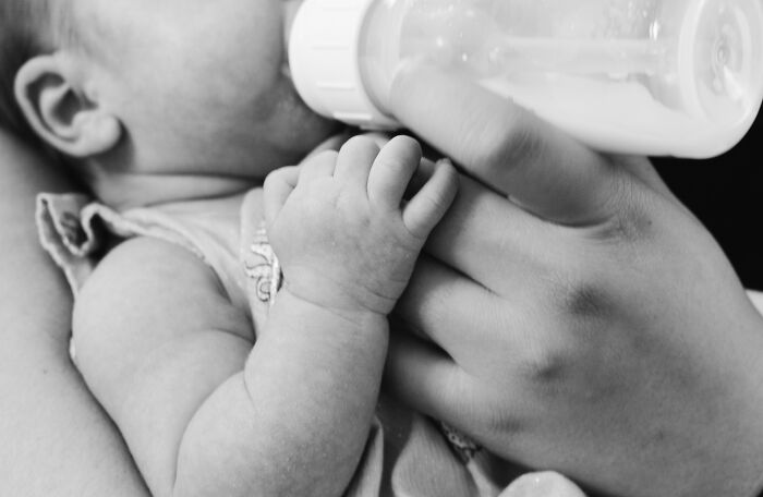 Baby drinking from a bottle, held by a person, illustrating a lifetime supply experience.