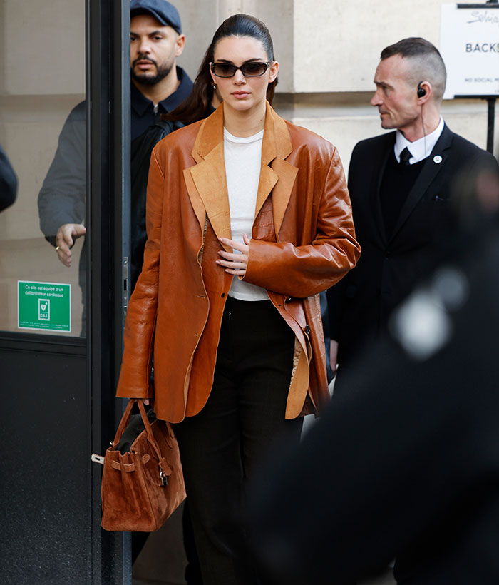 Kendall Jenner at Paris Fashion Week, wearing a stylish brown leather jacket and sunglasses.