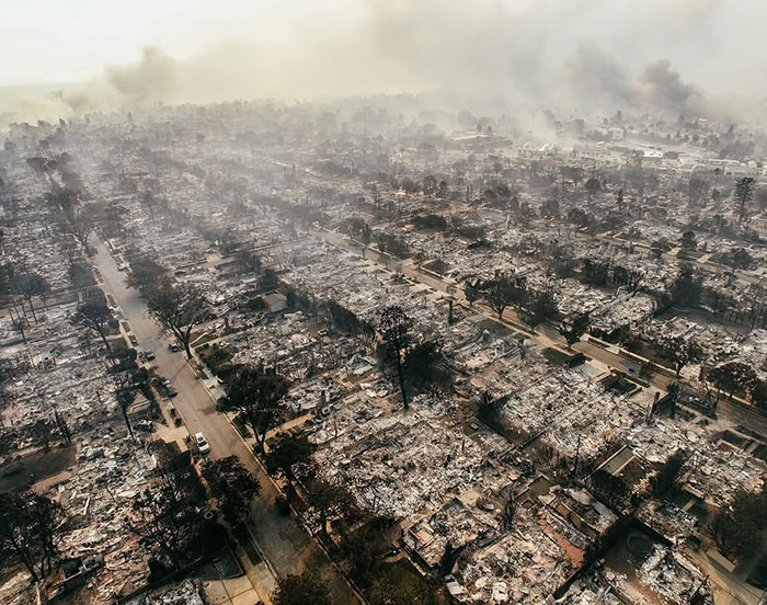 Aerial view of destruction from LA wildfires, smoke rising from burned buildings.