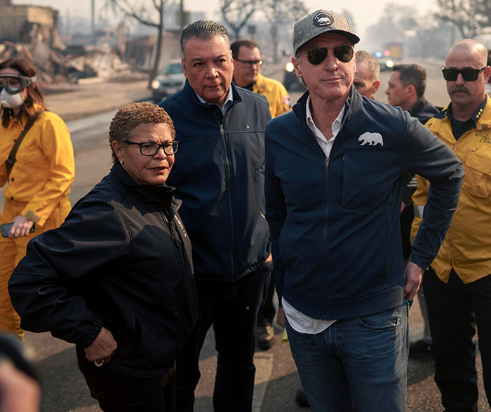 People in jackets surveying fire damage, with officials in yellow uniforms in the background.