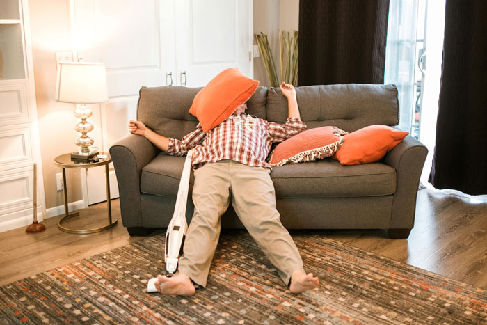 Man lounging on sofa with a vacuum cleaner, demonstrating weaponized incompetence in a living room setting.