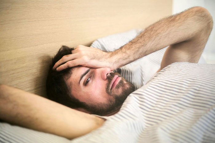 Man lying in bed, appearing frustrated, illustrating weaponized incompetence in relationships.