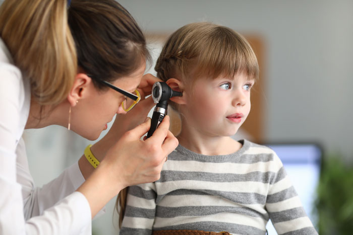 Doctor examining young girl's ear with otoscope in a medical setting.