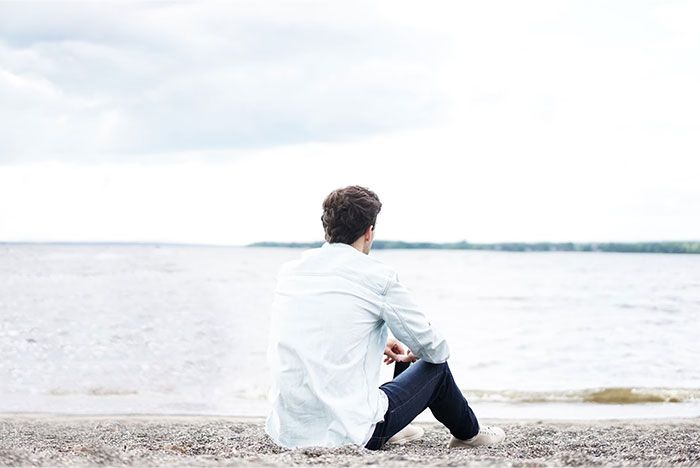 Person sitting on a beach in contemplation, gazing at the water, reflecting on wise observations.