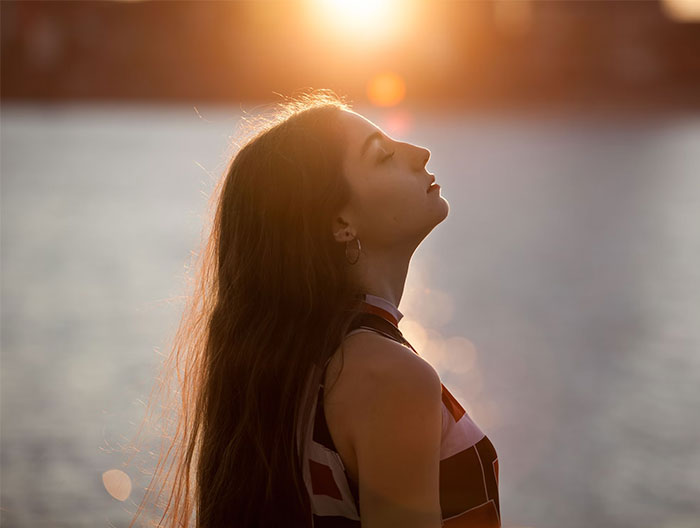 Young woman reflecting by a lake at sunset, embodying wise observations and introspection.