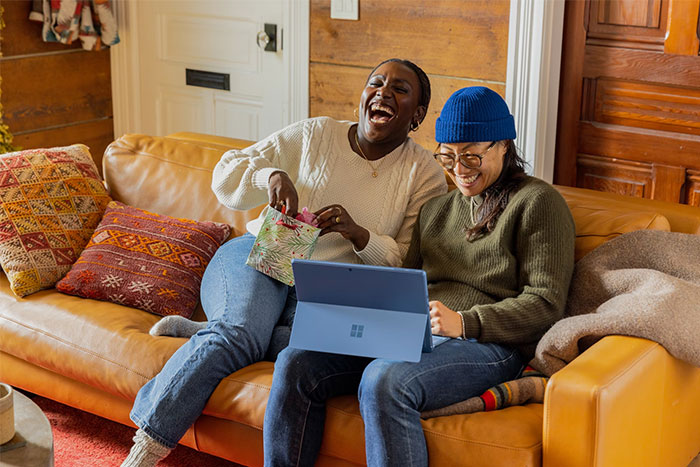 Two people laughing on a couch, one with a laptop, sharing wise observations and enjoying a casual moment.