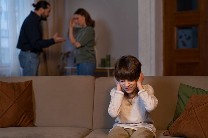 Child covering ears on a sofa while adults argue, illustrating wise observations on family dynamics.