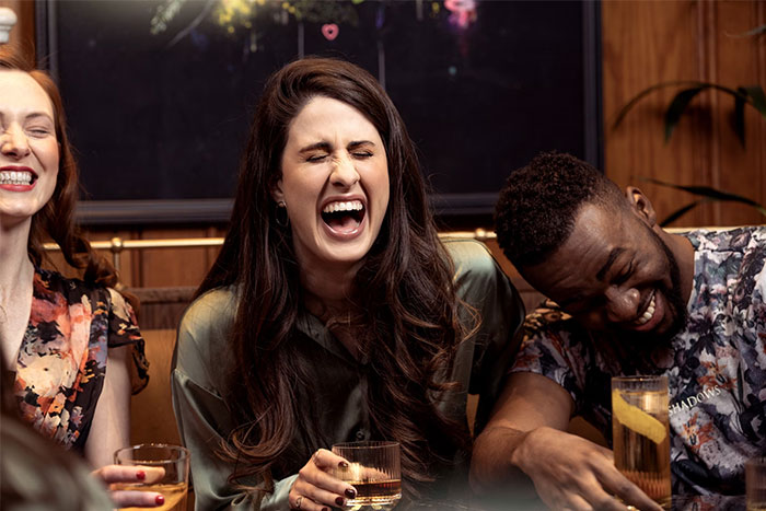 Three people laughing joyfully at a gathering, each holding a glass, capturing a moment of wise observations and shared insights.