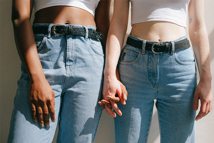 Two people wearing white tops and jeans, holding hands in natural light.