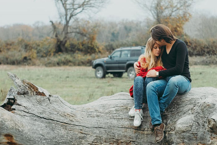 A person and a child sit together on a log in a field, sharing a moment of wise observation.