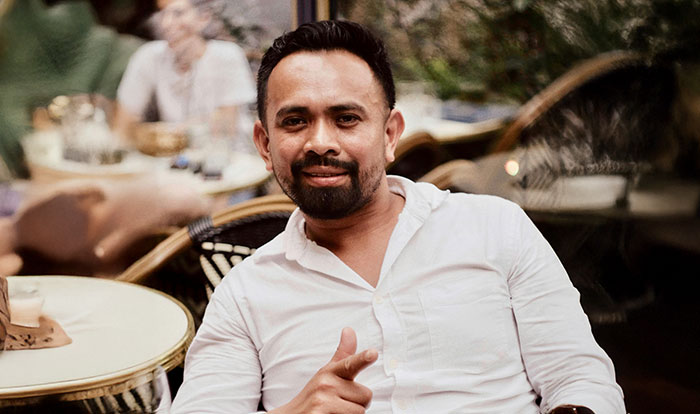 A man in a white shirt smiling and sitting at a cafe, embodying wise observations he wishes he'd known sooner.