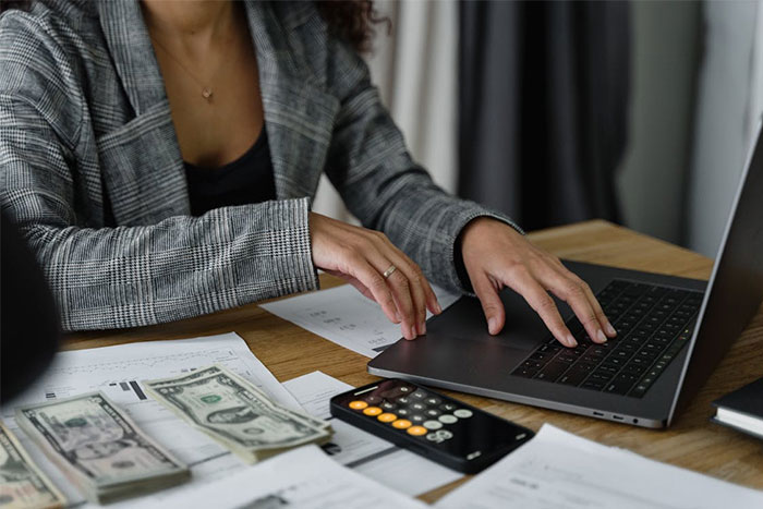 Person working at a desk with a laptop, calculator, cash, and papers, focusing on financial observations.