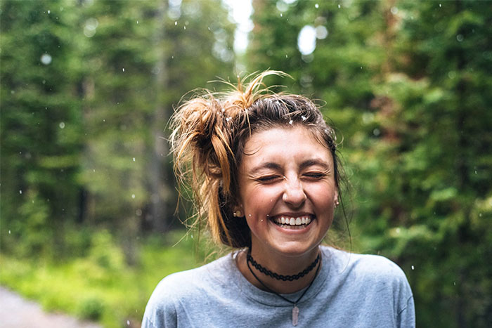 Woman smiling joyfully in a natural setting, embodying a wise observation about appreciating life.