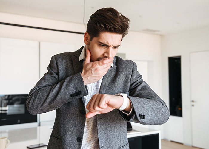 Man in a suit anxiously checking time on his watch, representing stress related to OCD and punctuality.