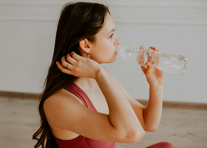 Woman in workout attire drinks water, embracing simple health hacks for better well-being.