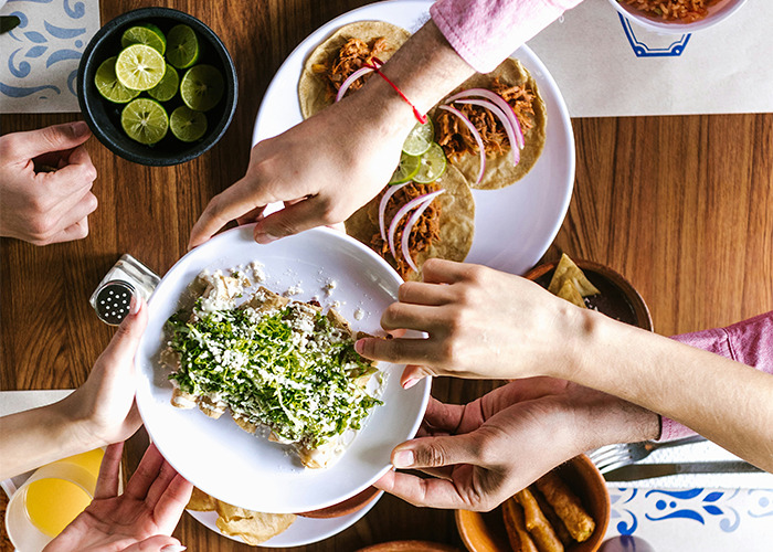 People sharing a meal with various dishes on a wooden table, highlighting community and healthy eating practices.