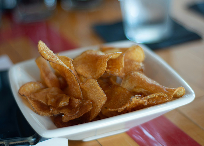 Bowl of crispy potato chips on a wooden table, illustrating a simple health hack of mindful snacking.