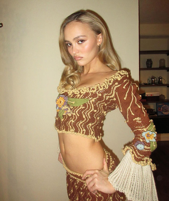 Blonde woman in a brown crochet outfit with floral details, posing indoors.