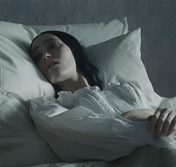 Young woman in a period costume lying in bed, emulating a scene from Nosferatu audition video.