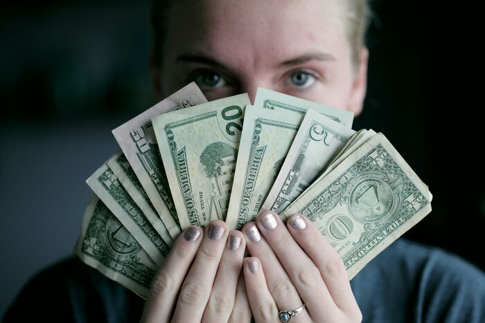 Person holding a fan of US dollar bills, symbolizing lottery wins and financial advice.