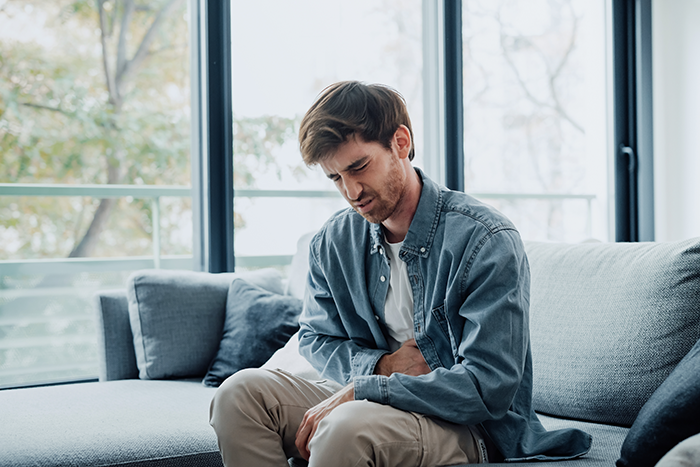 Man clutching stomach in discomfort on a sofa, illustrating effects of laxative in food incident.