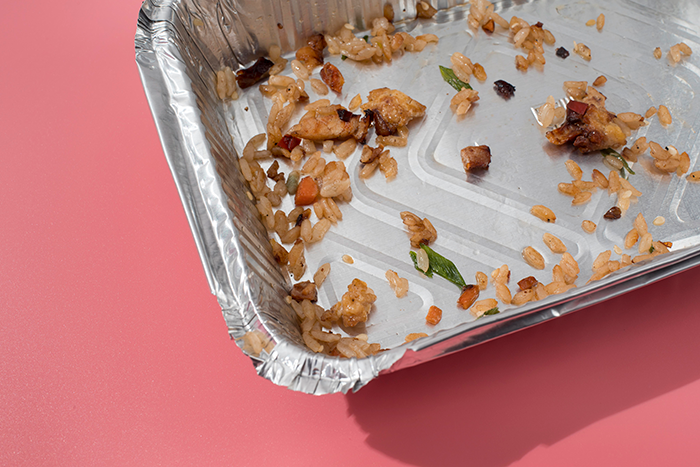 Empty foil tray with leftover food on pink background, related to office laxative incident.