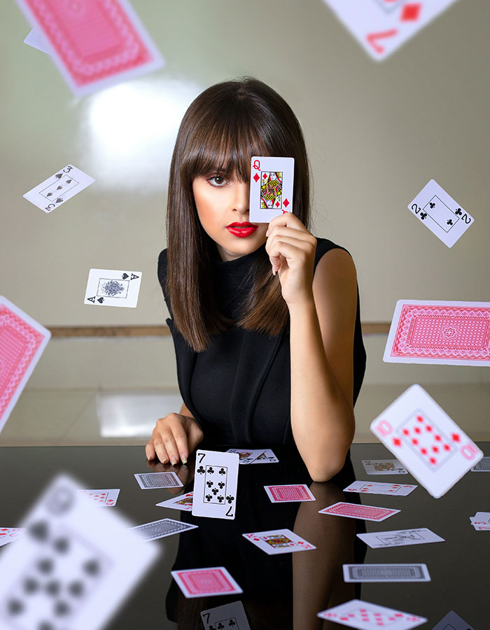 Freelance magician performing card trick, woman holding queen of hearts surrounded by floating playing cards.