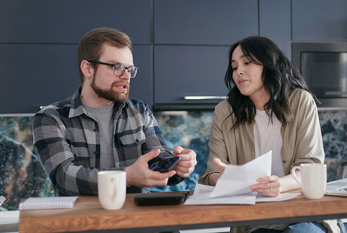 Man and woman discussing papers and phone over coffee at the kitchen table, related to infidelity accusations.