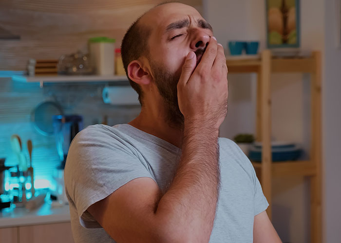 Man in kitchen yawning, contemplating decision after wife's C-section.