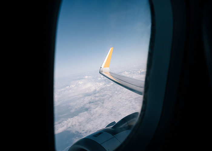 View from an airplane window showing a wing above the clouds, symbolizing travel choices and seat preferences.