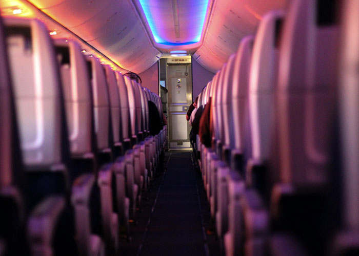 Airplane aisle view at night with seats illuminated by soft purple and orange lights.