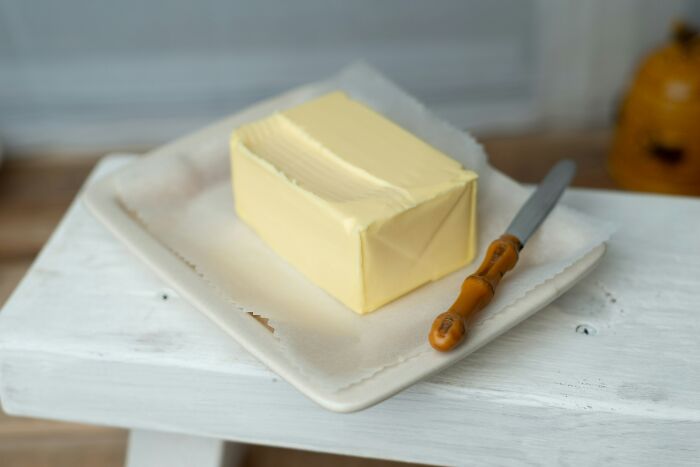 Block of butter on a plate with a knife, symbolizing expensive items worth spending money on in a gourmet kitchen setting.