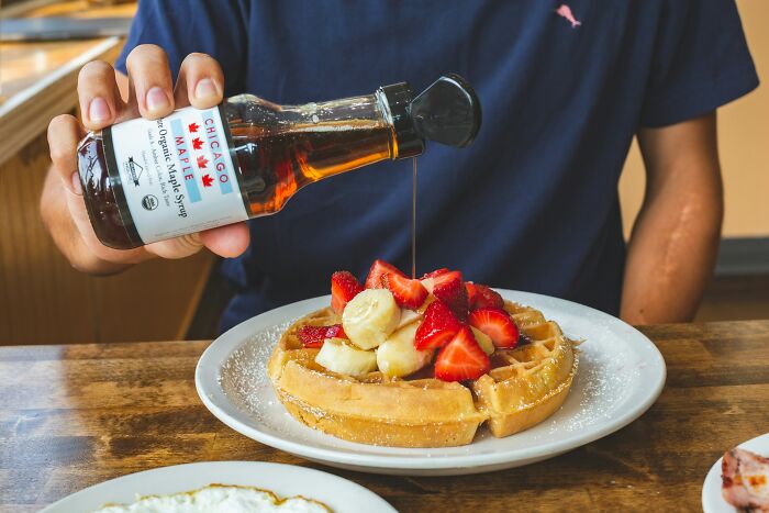 Person pouring maple syrup over gourmet waffles topped with strawberries and bananas, highlighting expensive items worth spending money.