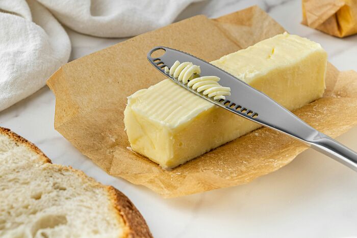 Butter stick on parchment with a serrated knife, symbolizing millennials approaching adulthood with unique challenges.