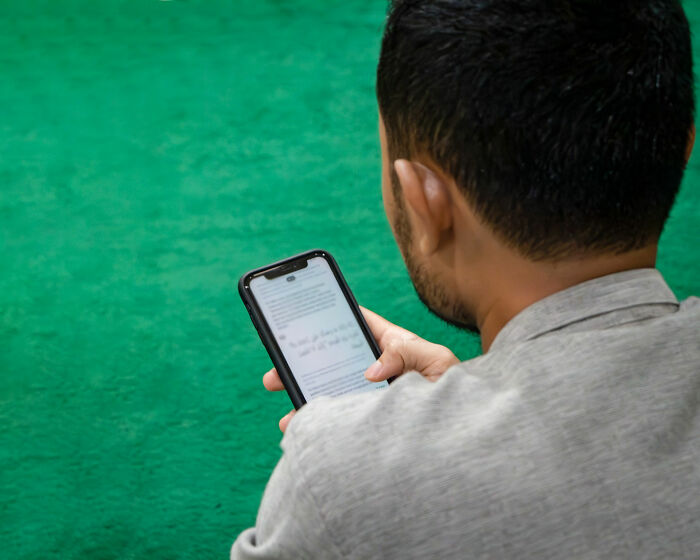 Man reading on smartphone, demonstrating one of the things that turn women on, while sitting on a green carpet.