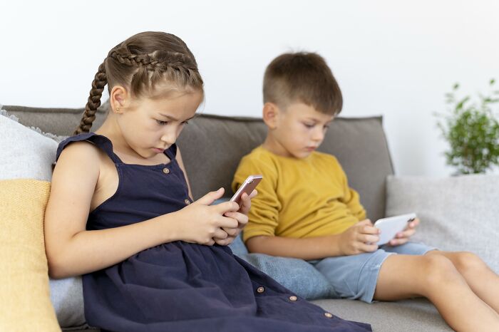 Children sitting on a couch, focused on smartphones, highlighting impact of phone addiction and parenting.