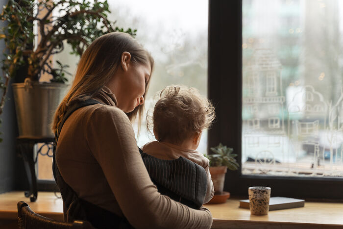 Woman holding a child by a window, illustrating kids feeling like foreigners in a different country.