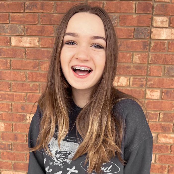 Teen girl smiling with braces, standing against a brick wall.