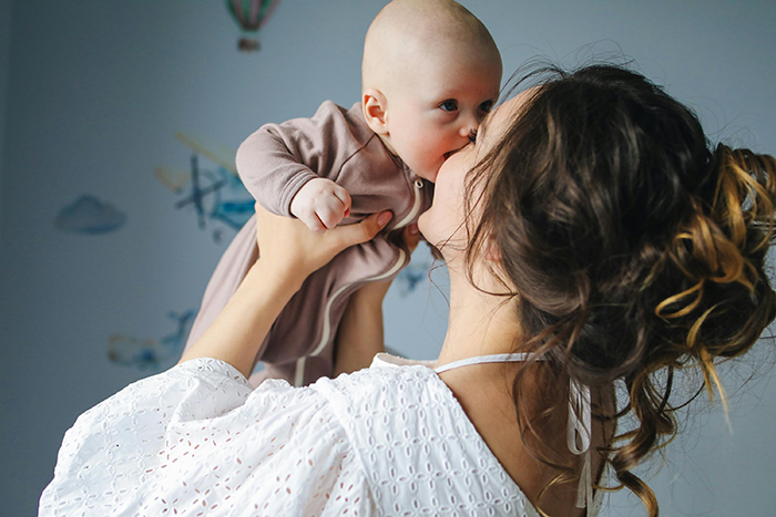 Woman holds baby up, both smiling, in a cozy room, highlighting family resemblance.