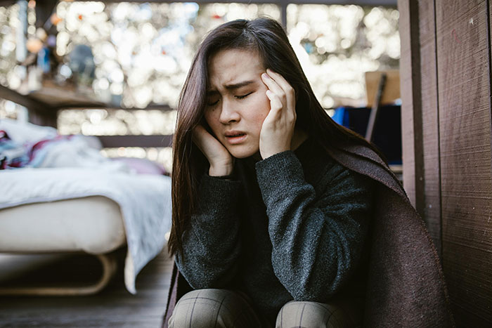 A person sitting on the floor, holding their head in distress, possibly due to mil threats or stress over a baby name.