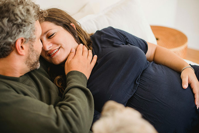 A couple embracing on a couch, the woman appears to be pregnant, symbolizing tender contact.