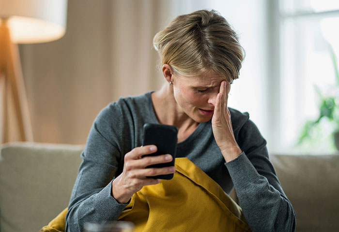 Stressed mom on couch, holding phone, refusing to pick up teens after clubbing.